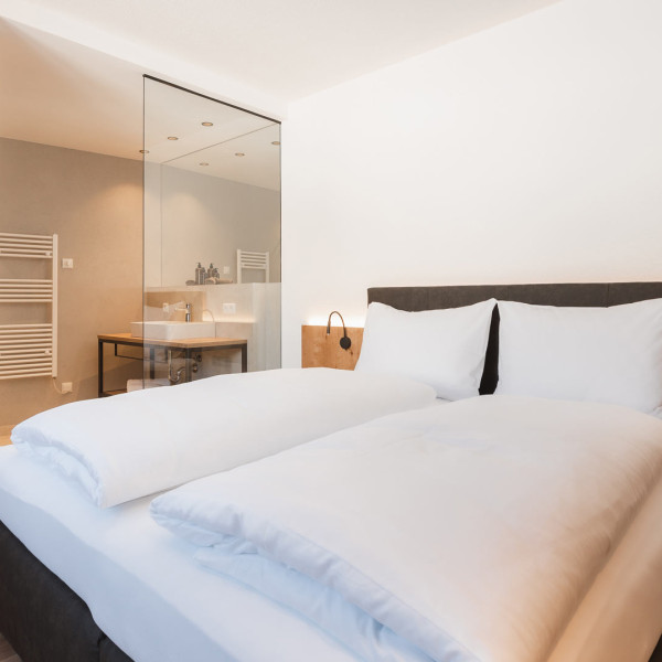 Alpina Serfaus, Doppelbett mit Blick in das offene Badezimmer