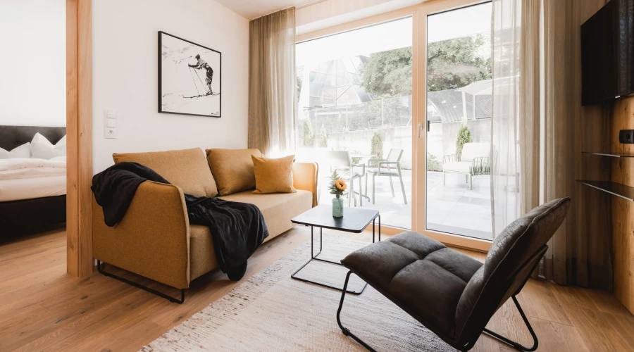 Apartment 104/204, Alpina Serfaus, Sofa mit modernem Stuhl und Blick auf die Terrasse